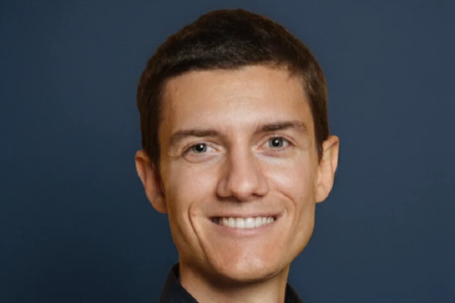 young man in black shirt against dark blue wall smiling